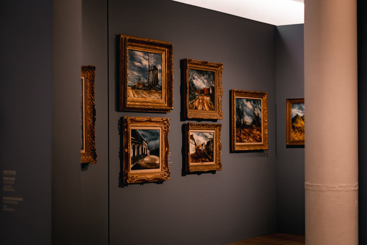 Elegant art gallery with framed paintings on a dimly lit wall, showcasing artistic works.